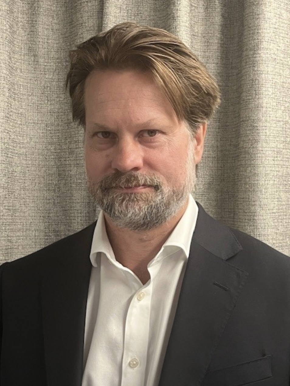 Headshot of a man wearing a white shirt and dark jacket.