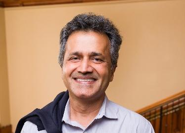 A man in a button-down shirt smiles against a neutral background.